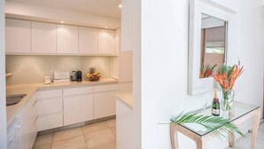 A modern kitchen with white cabinets and a glass table with a bottle and glasses. - Port Douglas Mirage Villa 123 (Port Douglas)