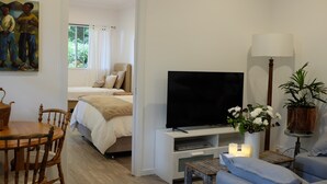 Ein modernes Wohnzimmer mit Flachbildfernseher, Esstisch mit Stühlen, Sofa, Lampe und Zimmerpflanze.