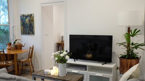 Ein Wohnzimmer mit Fernseher, einem Esstisch mit Stühlen, einem Couchtisch, einer Couch und einer Topfpflanze.