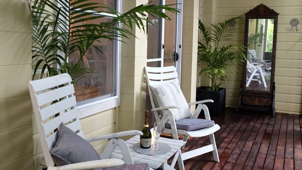 Eine überdachte Veranda mit zwei weißen Stühlen, einer Champagnerflasche und einem Spiegel.