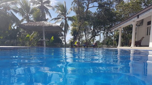 A clear blue pool surrounded by palm trees and a covered area with benches. - Tara Garden Tropical Villa with Private Pool & Friendly Staff Near Beach (Dharga Town)