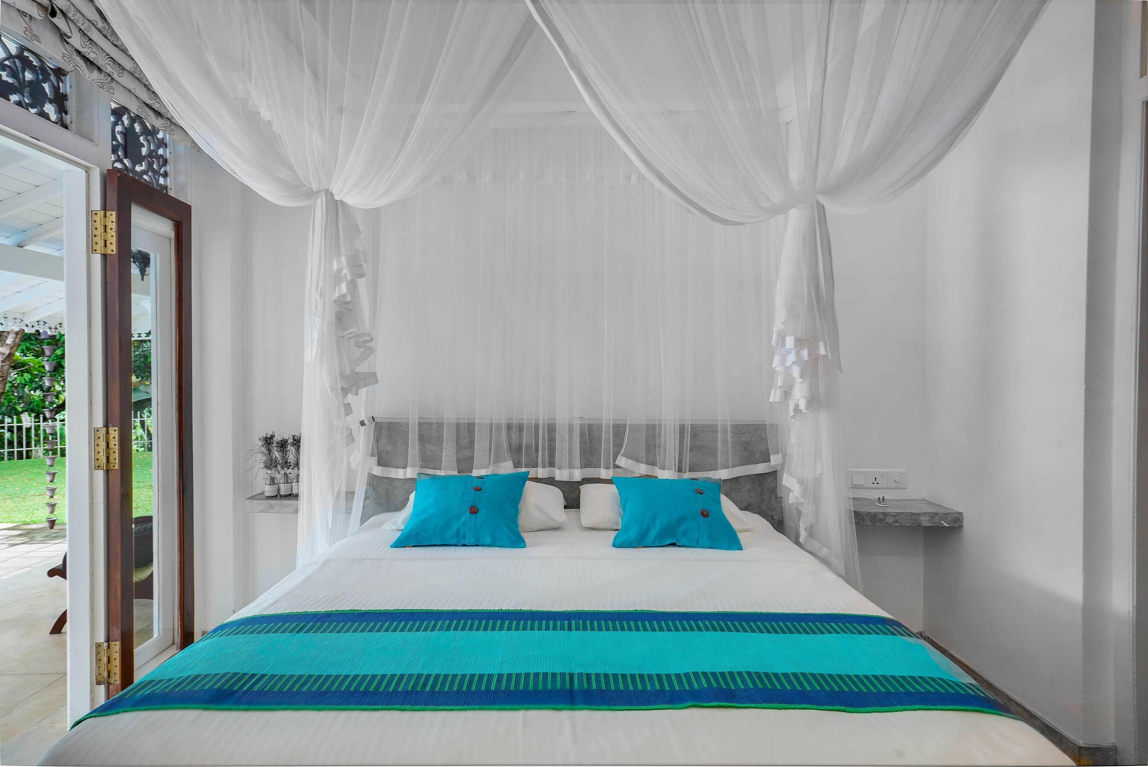 A bed with a white canopy, two blue pillows, and a teal and green striped bedspread.