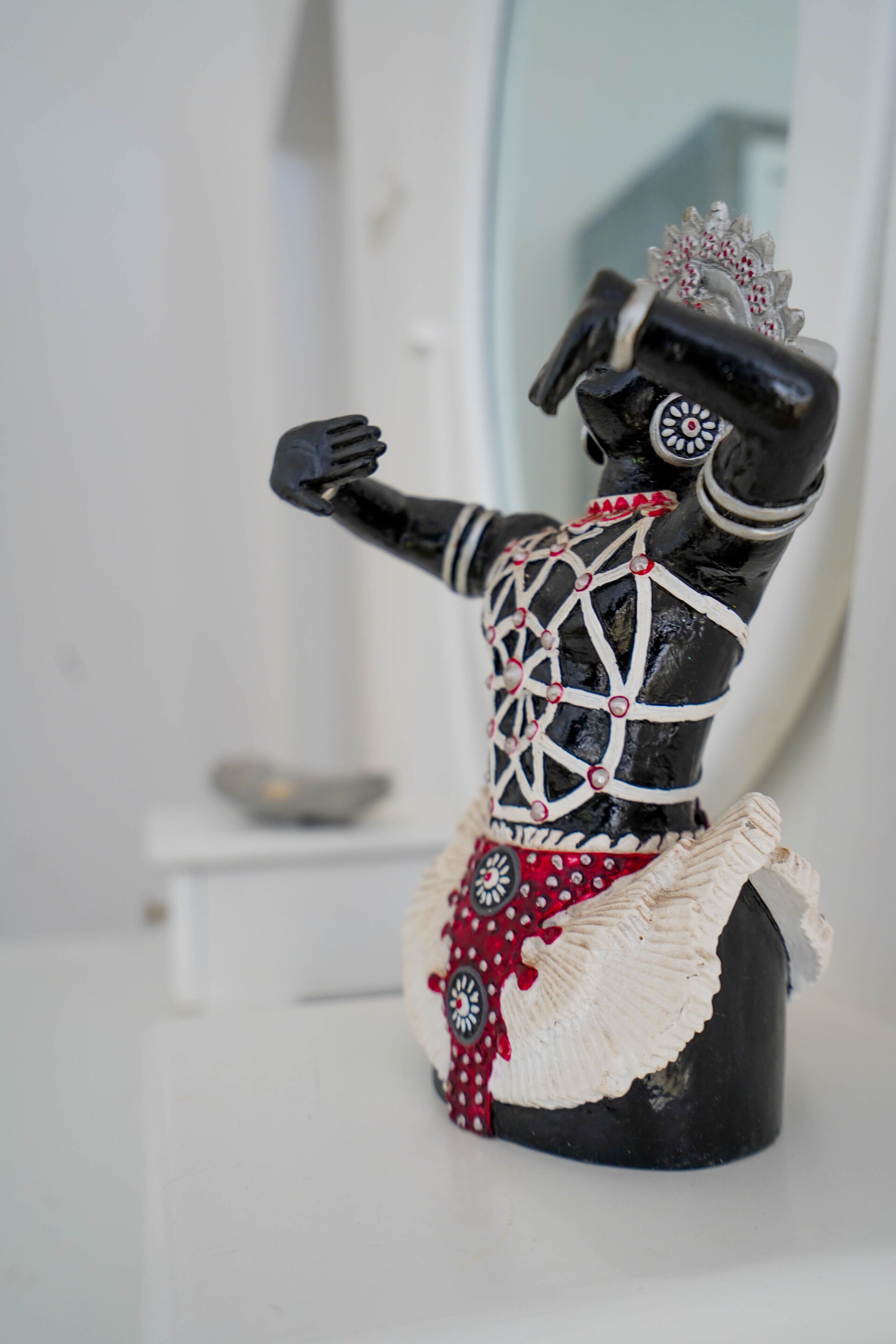 En liten statyett som föreställer en person klädd i en svartvit outfit med röda detaljer, placerad på en vit yta.