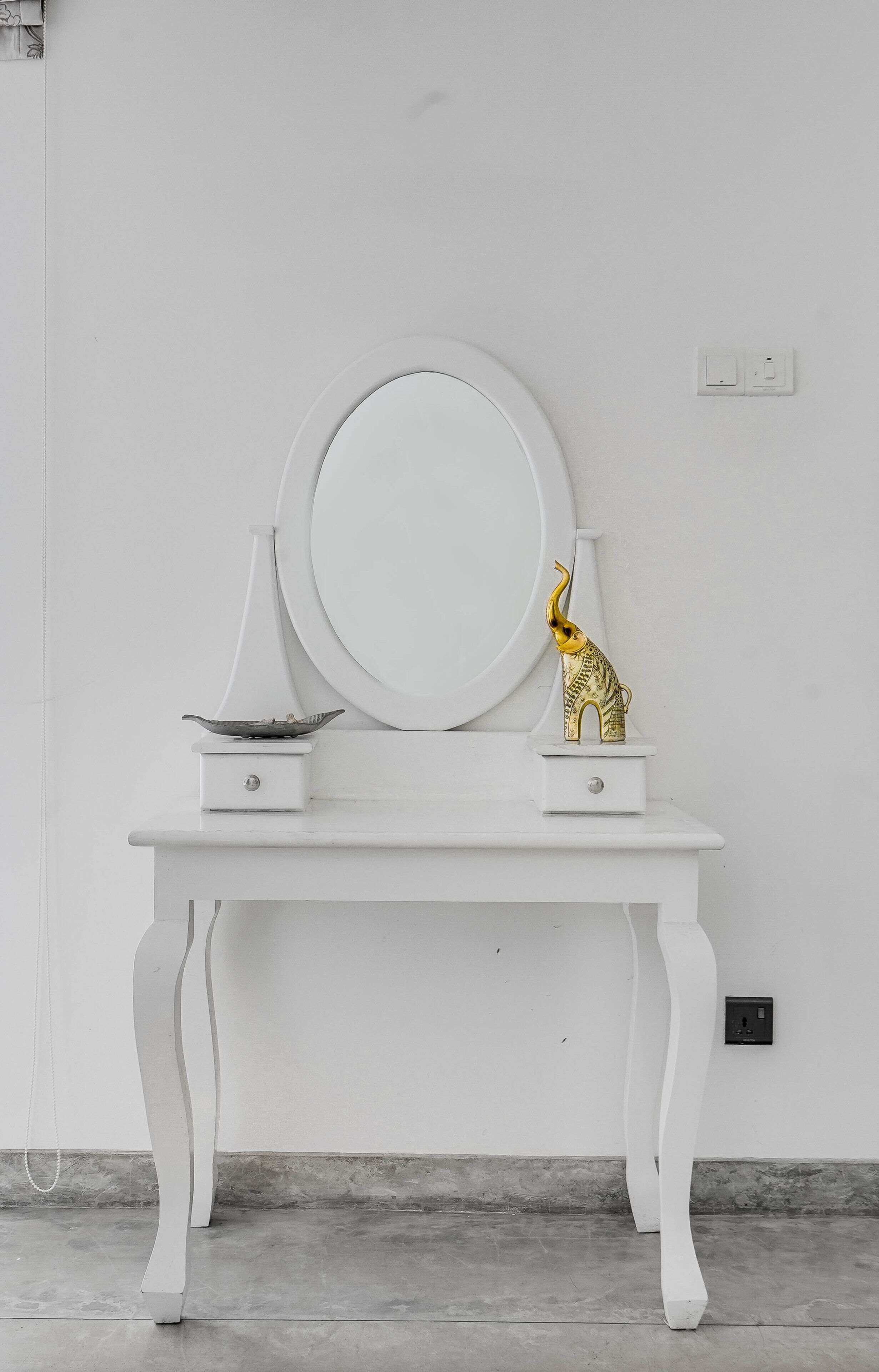 A white vanity with a round mirror, a small shelf with a decorative elephant figurine, and a bowl.