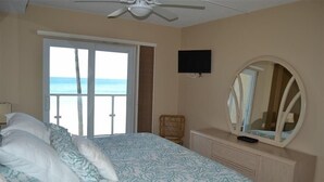 A bedroom with a bed, a television, a mirror, and a window with a view of the ocean. - Beachcomber unit 204 (Longboat Key)