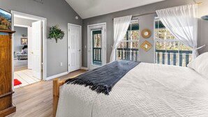 A bedroom with a large bed, a wooden headboard, a window with a view, and a door leading to another room.