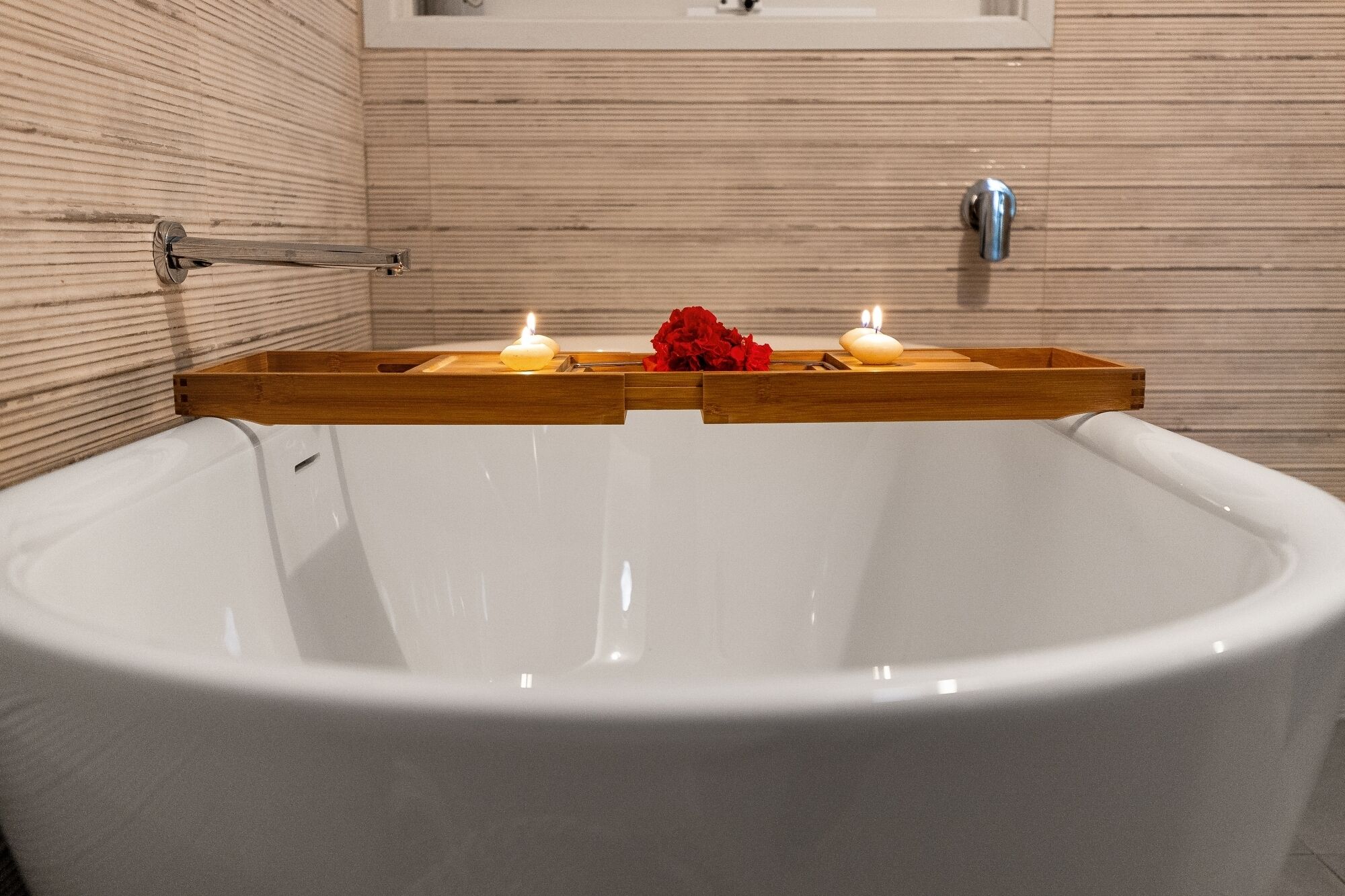 A modern bathroom with a large bathtub, wooden side panels, and two lit candles on a wooden tray.