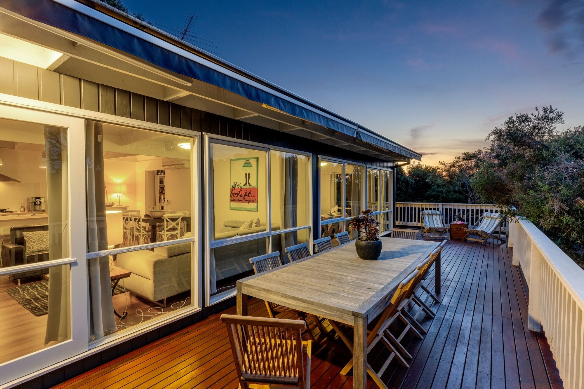 A modern house with a deck, large windows, and a dining area.