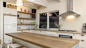 Une cuisine moderne avec des meubles blancs, un îlot central en bois et une cuisinière à gaz.