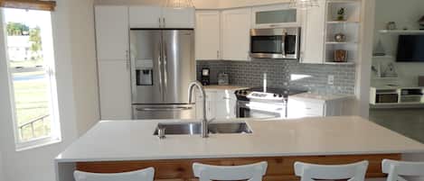 A modern kitchen with stainless steel appliances, a central island with bar stools, and a breakfast bar.