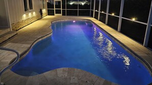 A swimming pool with a curved design, surrounded by a covered area with glass walls and stone flooring. - Beautiful house and great neighborhood! (Marco Island)
