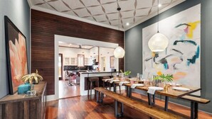 Un espace repas moderne avec des tables et des bancs en bois, une cuisine à l’arrière-plan et un grand tableau abstrait accroché au mur.
