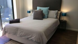 Ein ordentlich bezogenes Bett mit weißer Daunendecke, zwei Kissen und einem gefalteten Handtuch daneben. Auf beiden Seiten des Bettes stehen je eine Nachttischlampe.