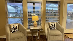 A living room with two armchairs, a small table with a lamp, and three windows with blinds. - Newly renovated- Panoramic Ocean Views Seconds to the Beach - Sandy Feet Retreat (Freeport)