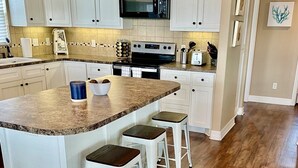 A kitchen with white cabinets, a granite countertop, a microwave, a stove, and three bar stools. - Newly renovated- Panoramic Ocean Views Seconds to the Beach - Sandy Feet Retreat (Freeport)