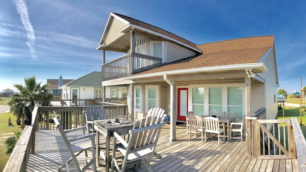 A two-story house with a deck, a red door, and a covered outdoor seating area with chairs and a table. - Newly renovated- Panoramic Ocean Views Seconds to the Beach - Sandy Feet Retreat (Freeport)