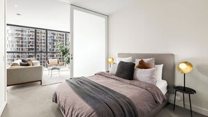 Un dormitorio moderno con una cama grande, dos lámparas de noche, un sofá y vistas a la ciudad a través de ventanales del suelo al techo.