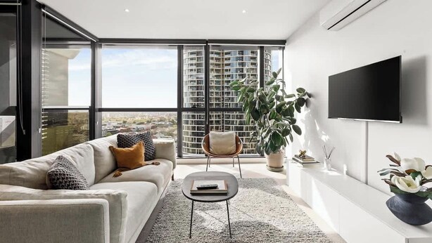 Una sala de estar moderna con un sofá, una mesa de centro, un televisor y un ventanal con vistas a edificios altos.