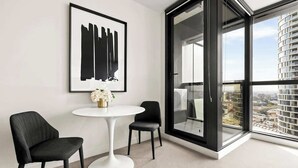 Una habitación moderna con un ventanal grande, una mesa redonda blanca, dos sillas negras y una obra de arte enmarcada en la pared.