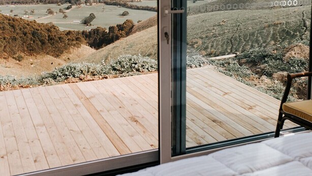Une chambre dotée d’une grande porte-fenêtre coulissante qui donne sur une terrasse offrant une vue sur un paysage rural.