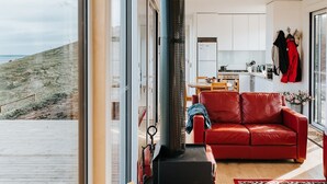 Un salon moderne avec un canapé en cuir rouge, une cheminée et une vue sur la plage grâce à de grandes portes-fenêtres coulissantes.