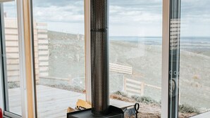 Un salon moderne doté d’une grande porte vitrée donnant sur un balcon, d’un poêle à bois noir et d’un pouf en cuir rouge.