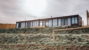 Un bâtiment moderne doté de grandes fenêtres et d’un toit plat, entouré d’une clôture et d’une végétation clairsemée.