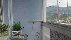 En balkong med ett bord och stolar, krukväxter och utsikt över en byggnad med skylten ”Slovenska”.