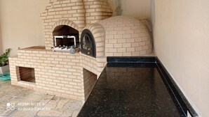 En udendørs ovn i mursten med en sort bordplade og et vindue, sandsynligvis til pizza eller madlavning.