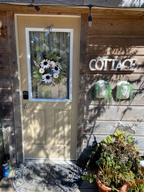 A wooden cottage entrance with a door, a welcome sign, and a 'COTTAGE' sign.