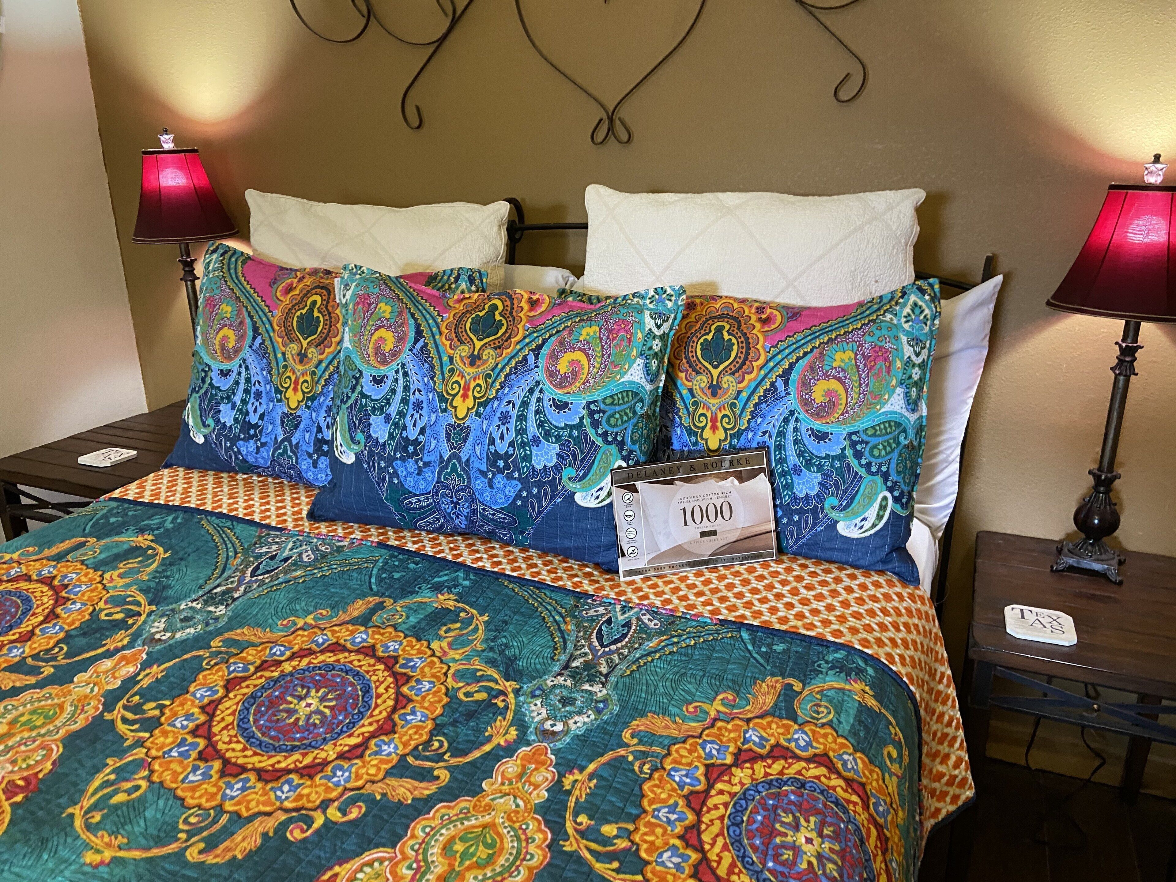 Un lit avec une literie colorée et à motifs, et deux lampes de chaque côté.