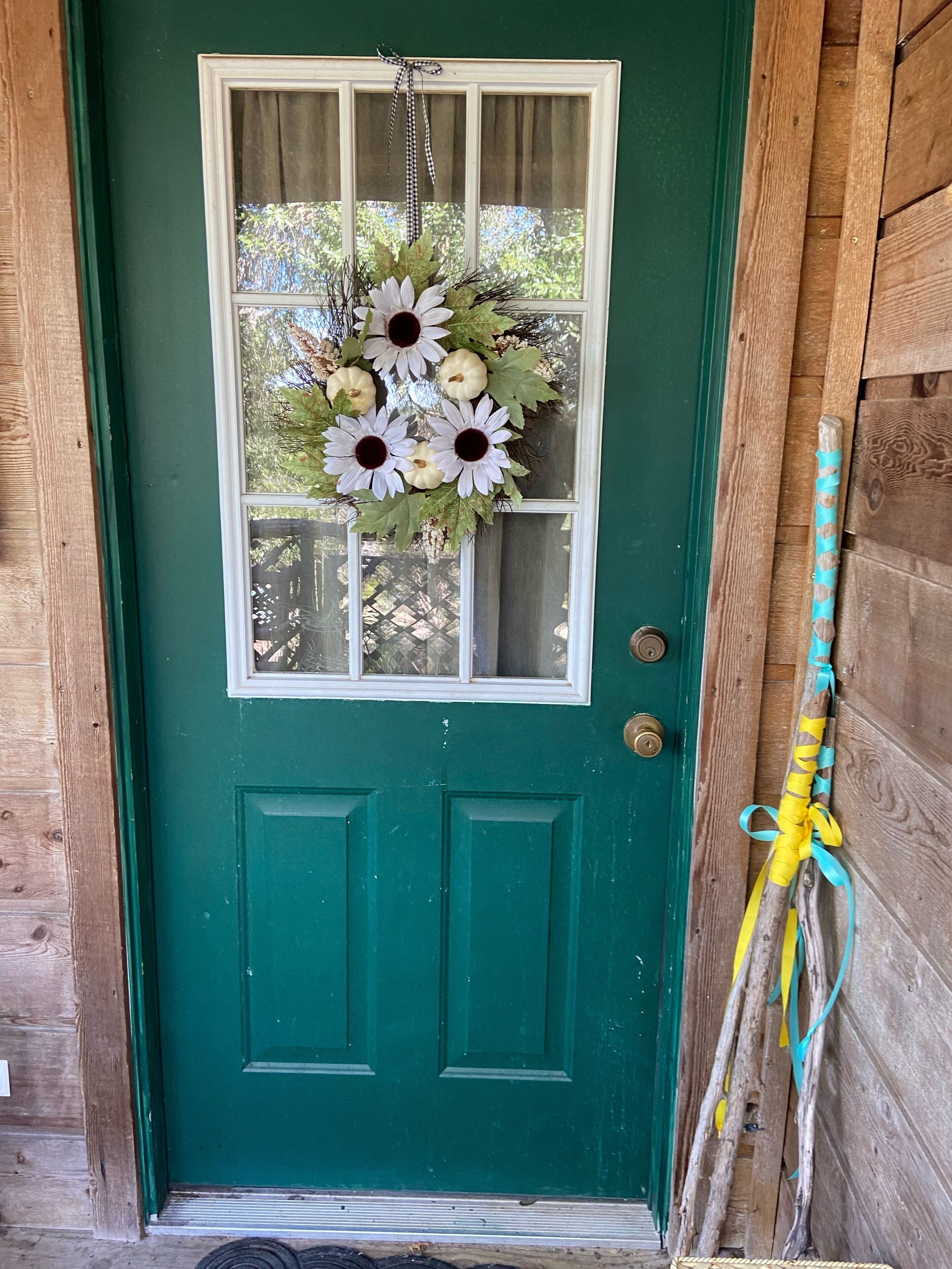 Une porte verte avec une fenêtre, une couronne décorative et un cadre de porte en bois.