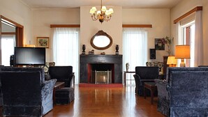 Un salon spacieux avec une cheminée, deux fauteuils, un canapé, une télévision et un lustre.