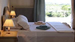Une chambre d’hôtel avec un lit, deux lampes de chevet, un téléphone et une vue sur la verdure par la fenêtre.
