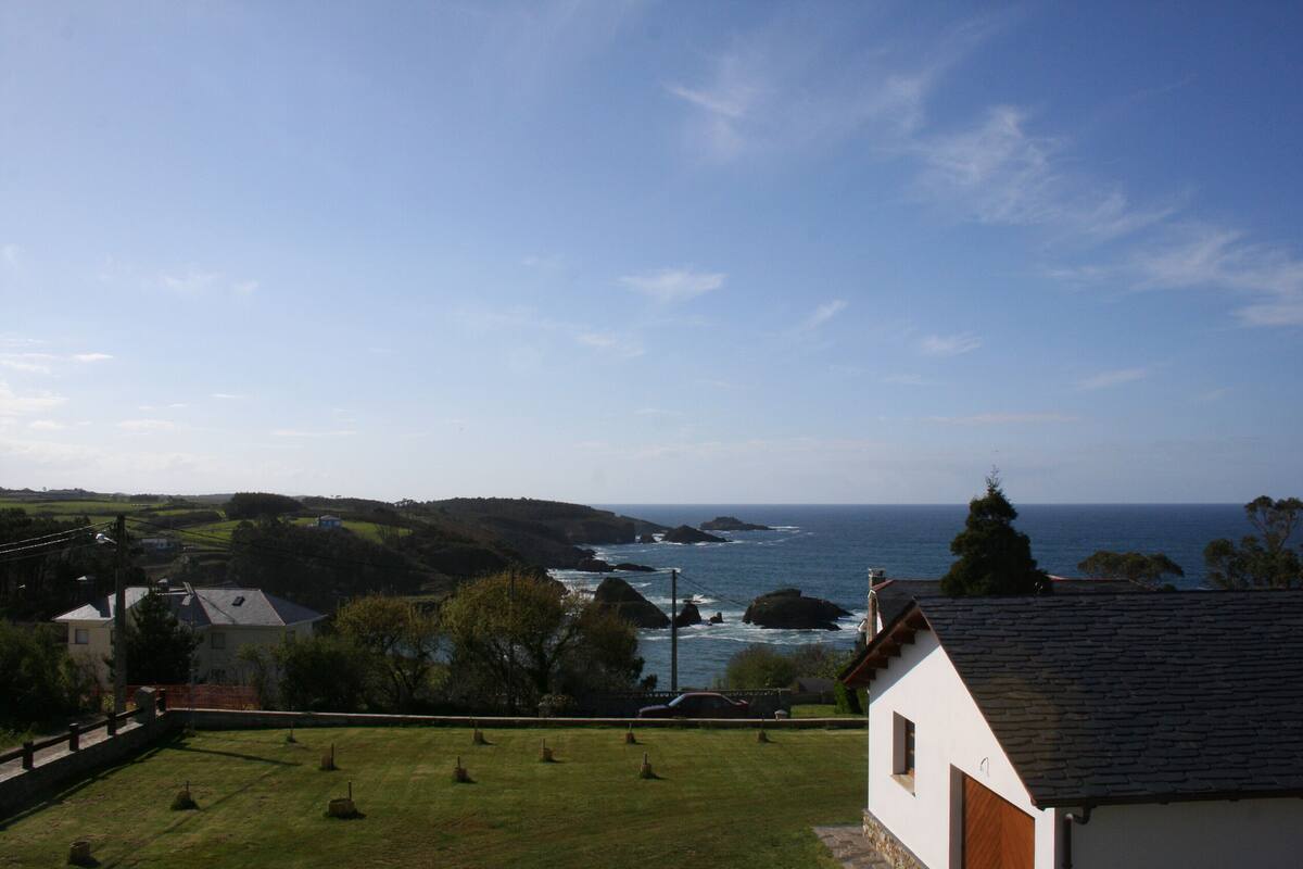 A coastal view with a grassy area, a white building with a tiled roof, and the ocean in the background.