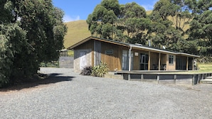 A building with a gravel driveway and a wooden deck. - Relax Beachside with your Family and Friends (Oakura)