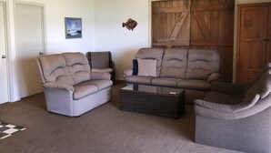 A living room with two grey sofas, a wicker coffee table, and a wooden barn door. - Relax Beachside with your Family and Friends (Oakura)