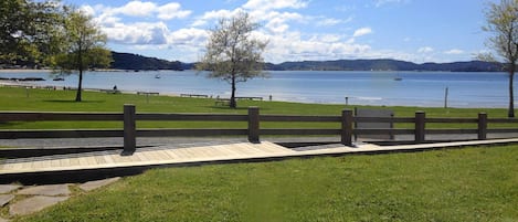 A park with a wooden deck, grassy areas, and a lake with boats.