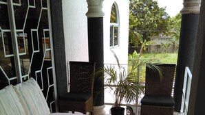 Ein Zimmer mit einem Bett, zwei Korbstühlen, einer Topfpflanze und Blick auf Grünflächen.