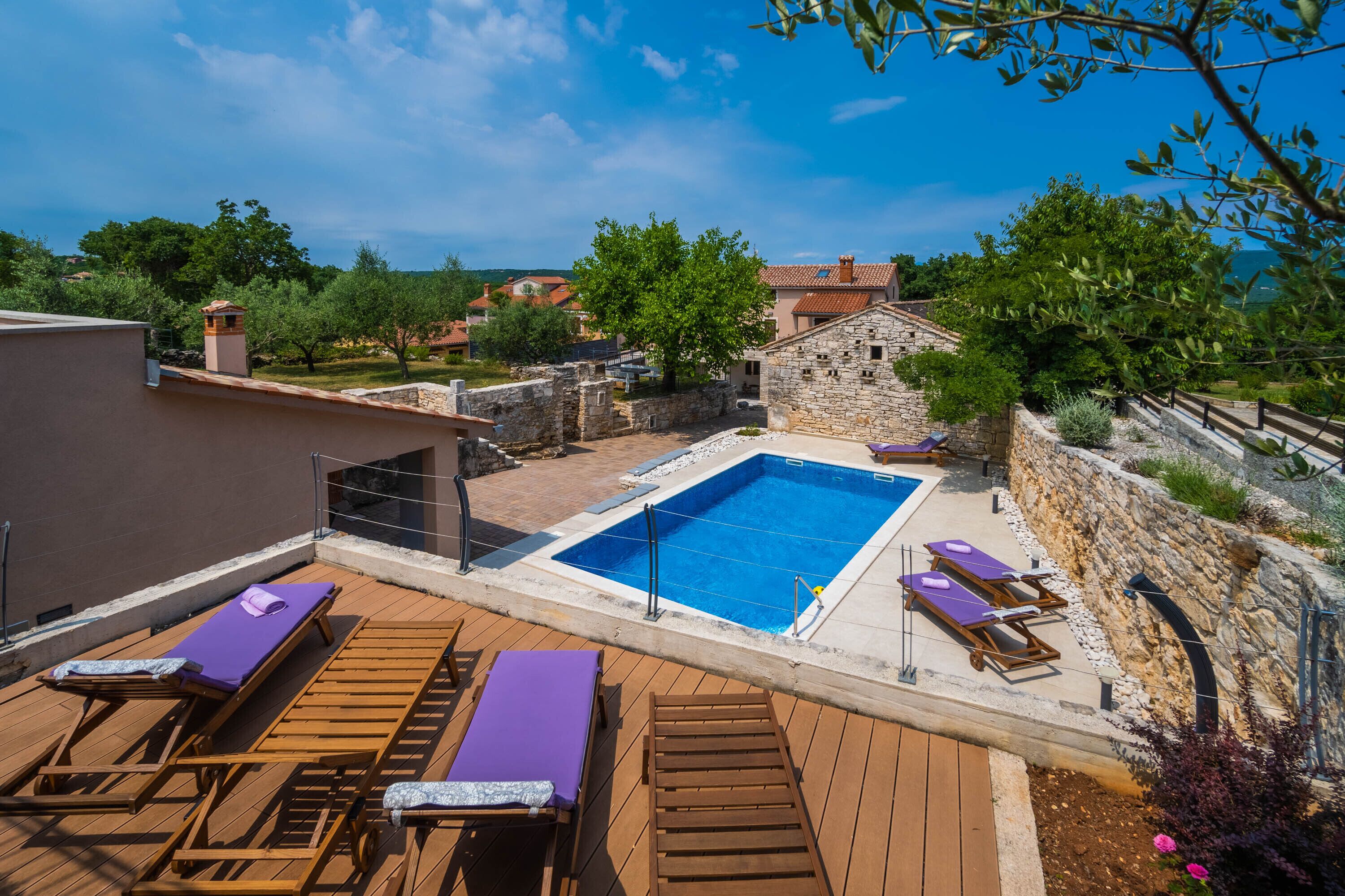 A rooftop pool area with wooden loungers and a stone wall.