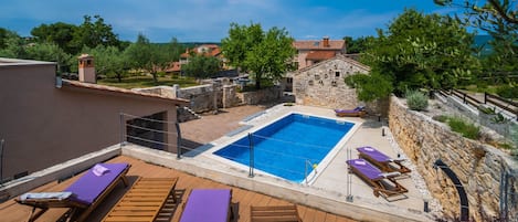 A rooftop pool area with wooden loungers and a stone wall.