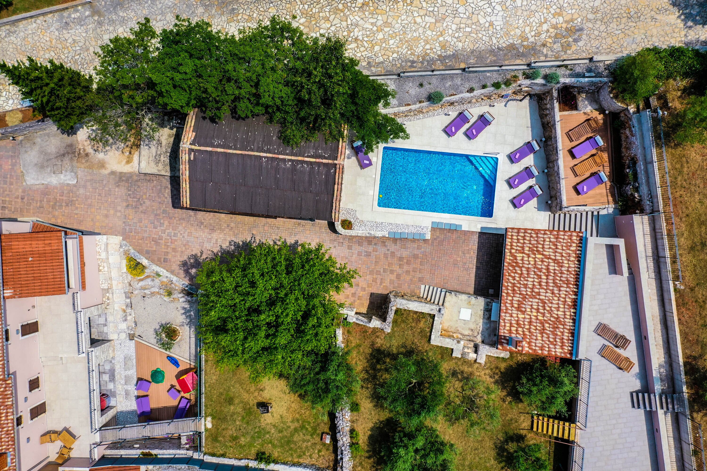 Vista aérea de una propiedad con piscina, mobiliario exterior y vegetación circundante.