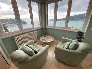 Une chambre d’angle avec vue sur la mer, deux fauteuils, une petite table ronde et un radiateur.