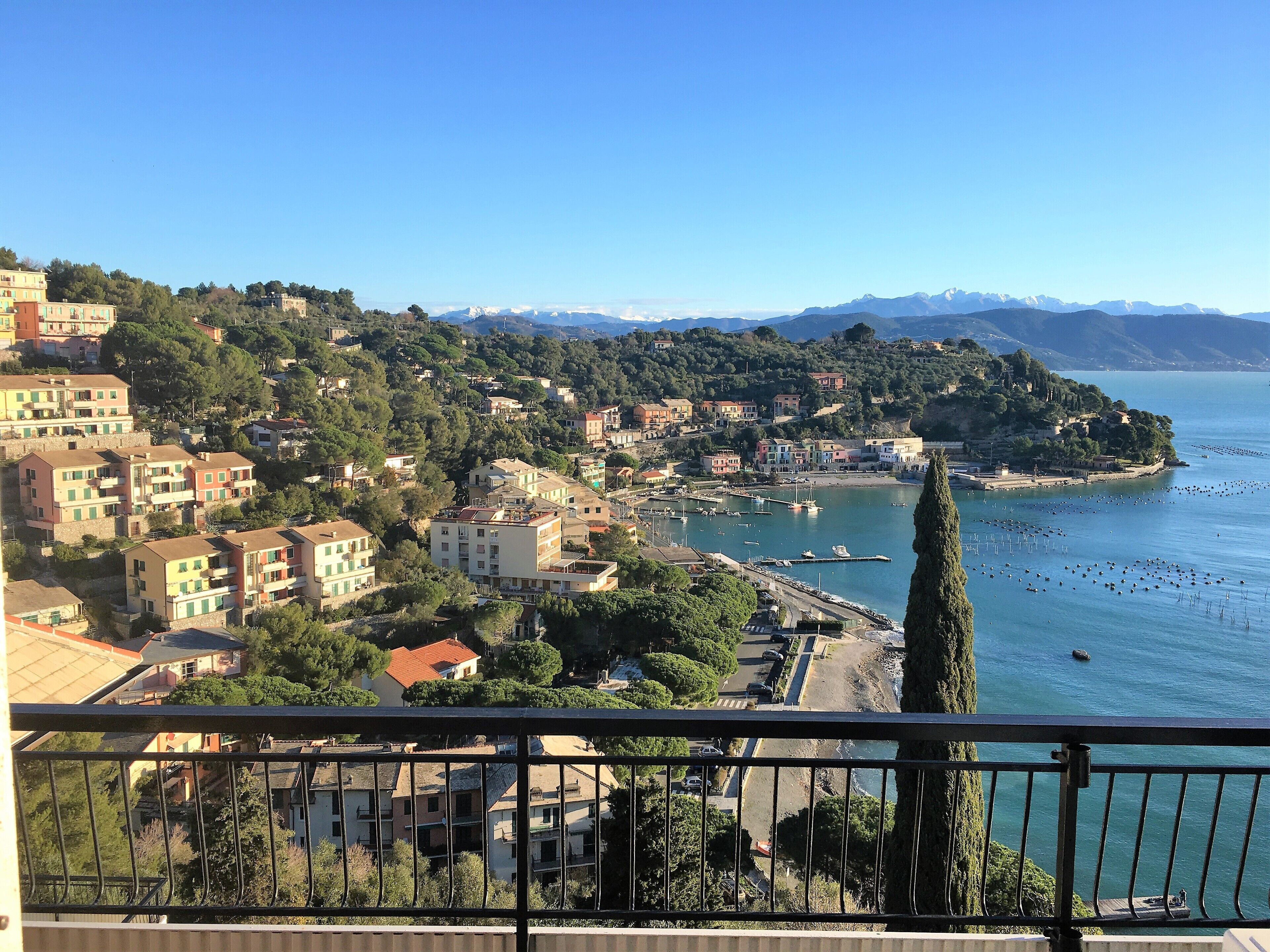 A coastal town with buildings, a marina, and a view of the sea and mountains.