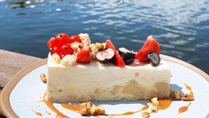 A dessert on a plate with a body of water and boats in the background. - Hotel Port 110 (Ilawa)