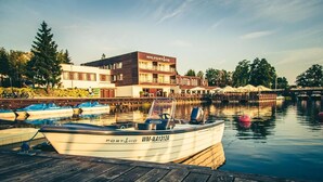 A waterfront hotel with a docked boat, a wooden pier, and a building with a sign reading 'HOTEL PORT'. - Hotel Port 110 (Ilawa)