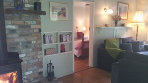 A cozy living room with a brick fireplace, a bookshelf, a bed, and a sofa. - ROSE AT LEAFIELD COTTAGES (Dixons Creek)