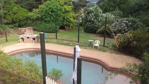 A swimming pool with a brick patio, surrounded by a fence and lush greenery. - ROSE AT LEAFIELD COTTAGES (Dixons Creek)