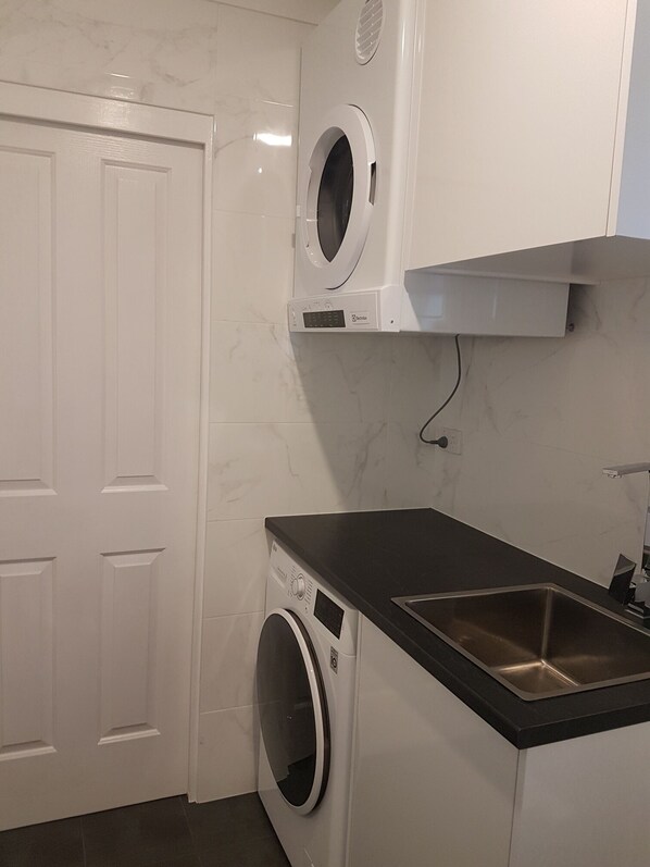 A compact laundry room with a washing machine, a dryer, and a sink. - A home away from home (Glenwood)