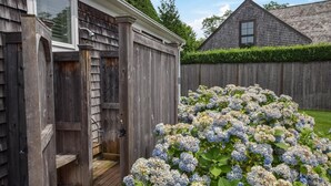 A wooden shed with a door and a small porch, surrounded by a wooden fence and a large bush of hydrangea flowers. - 1 min drive to Rock Harbor, 2 min to Town! (Orleans)